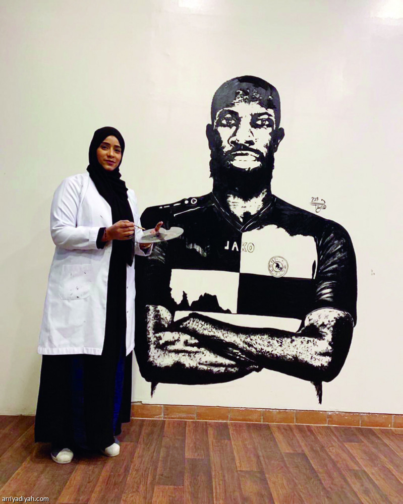 صورة التقطت لليلى القلاف أمام لوحة جدارية في المركز الإعلامي في نادي الاتفاق رسمت فيها السنغالي سليمان دوكارا (الرياضية)